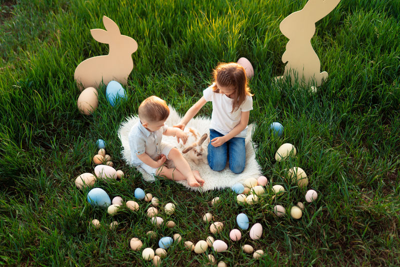小女孩和男孩玩兔子。快乐的小女孩抱着可爱的毛茸茸的兔子。与复活节兔子的友谊。春拍美女少年抱兔