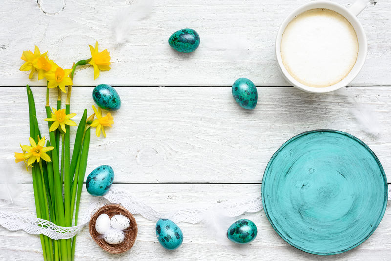 复活节背景，有复活节彩蛋、春花、一杯卡布奇诺和空的蓝色盘子