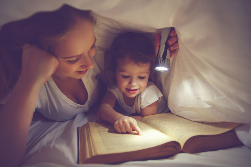 家庭阅读就寝时间。带闪光灯的妈妈和孩子读书