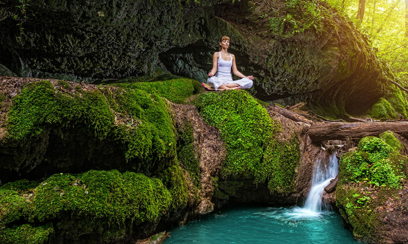女人在大自然中练习瑜伽，瀑布。sukhasana姿势