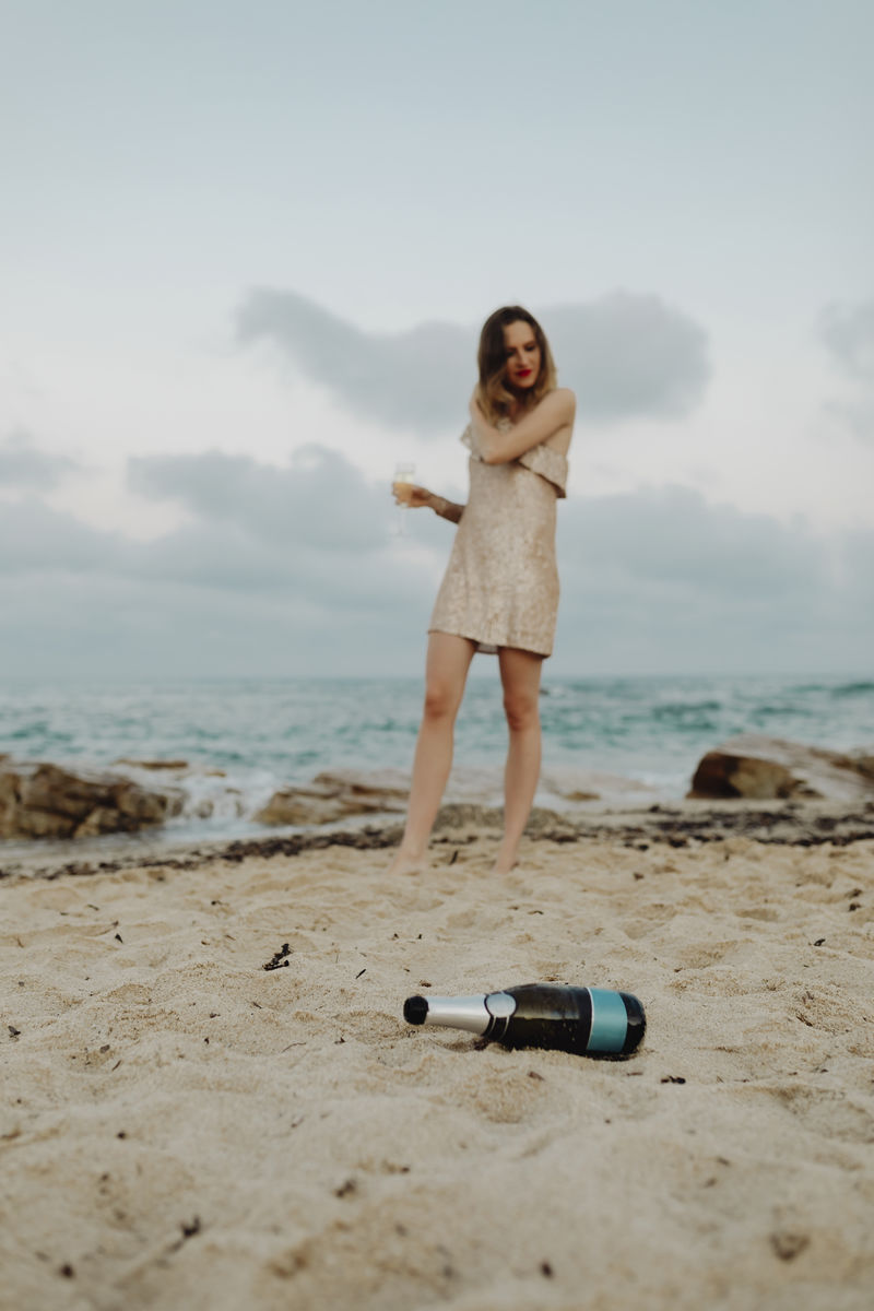 一个穿着金色裙子的女人在沙滩上喝着香槟