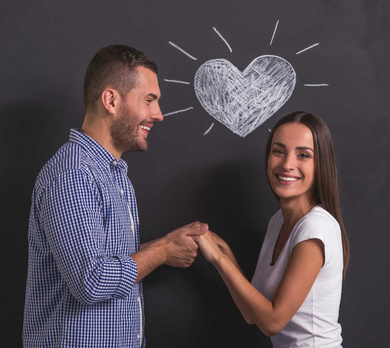 美丽的年轻夫妇手拉着手微笑着站在黑板上