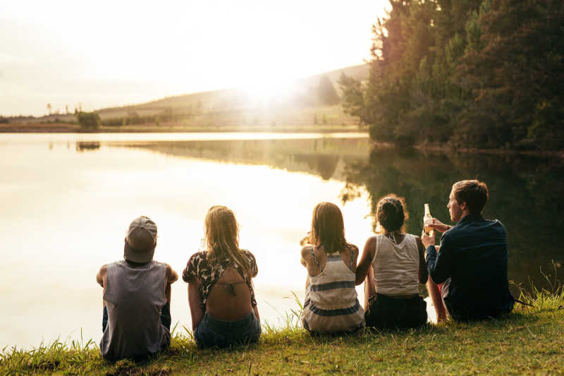一群年轻男女坐在草地上看向湖边的夕阳余晖