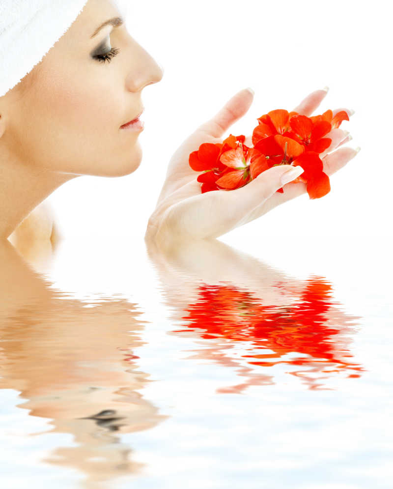 可爱的女人带着红色的花瓣在水中