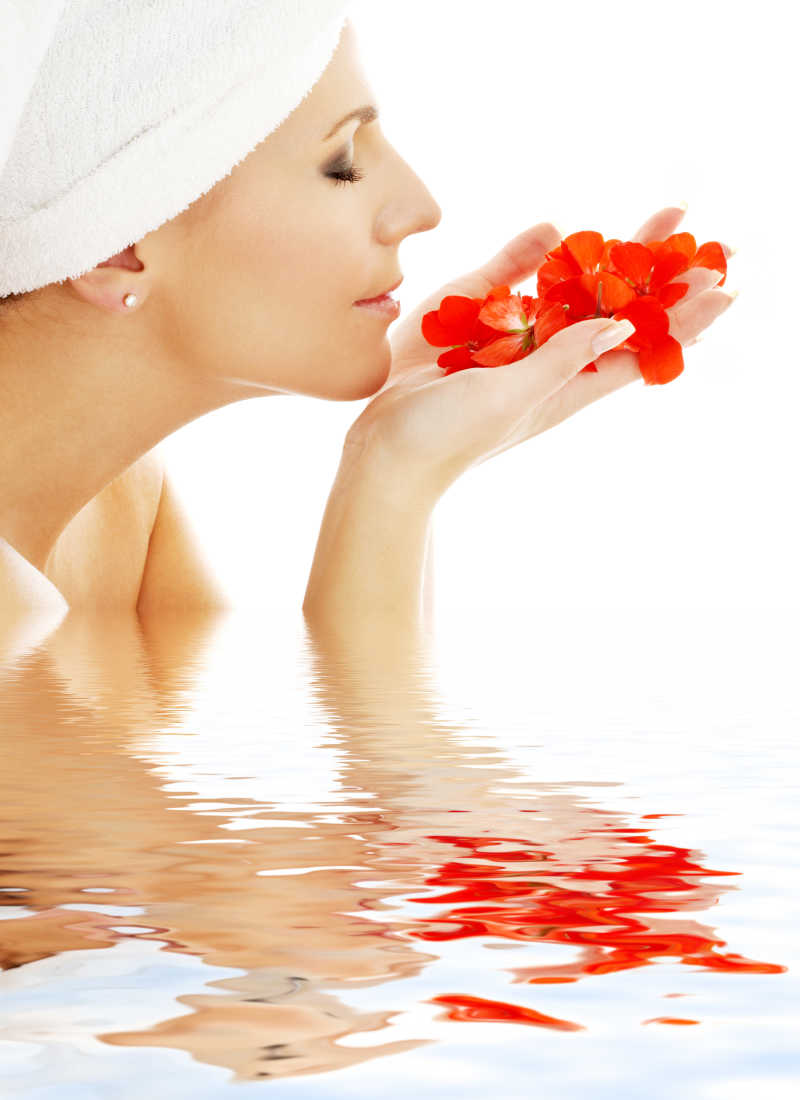 在水中闻到红色的花瓣的可爱的女人