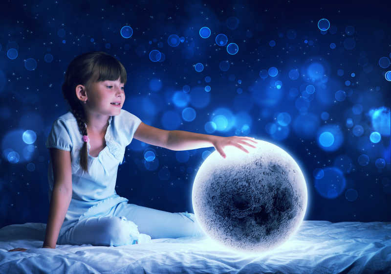 可爱的女孩在床上看着发光的月亮星球