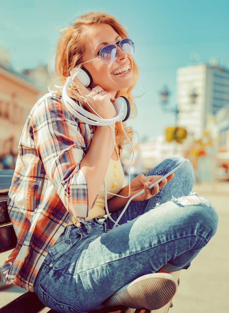 坐在街边拿着耳机听音乐的女人