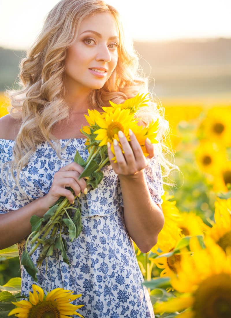 阳光照射下的金发美女拿着向日葵花