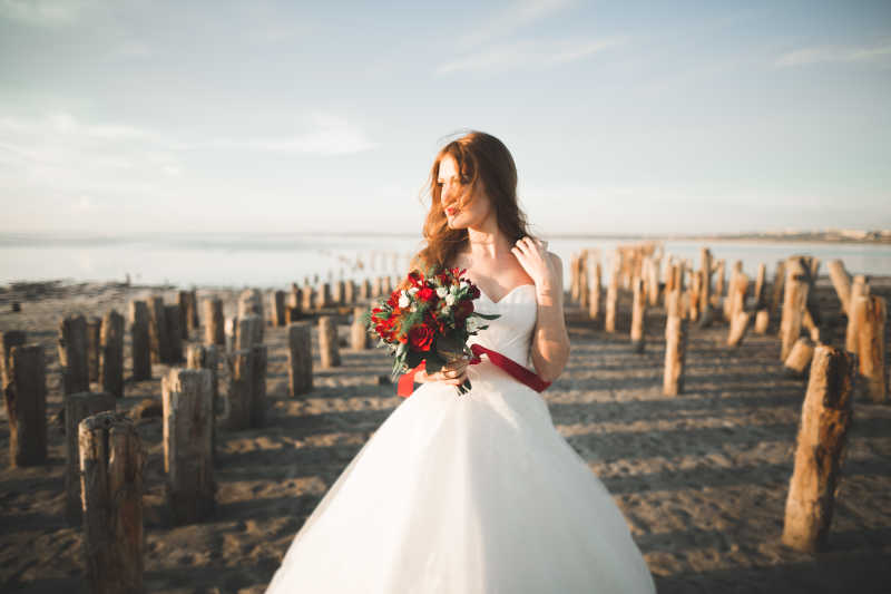 穿着白色婚纱站在海滩上的美丽新娘