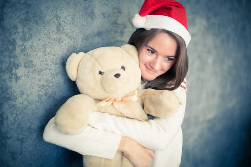 带着圣诞帽抱着小熊微笑的女孩