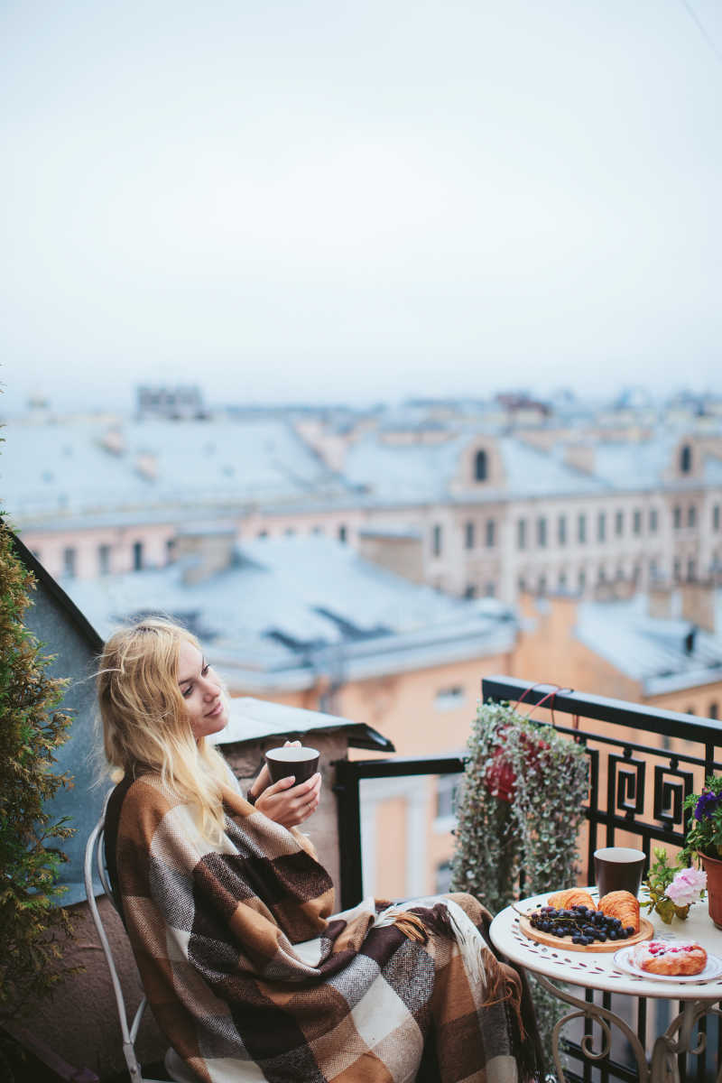 建筑背景下在阳台上喝咖啡的金发美女