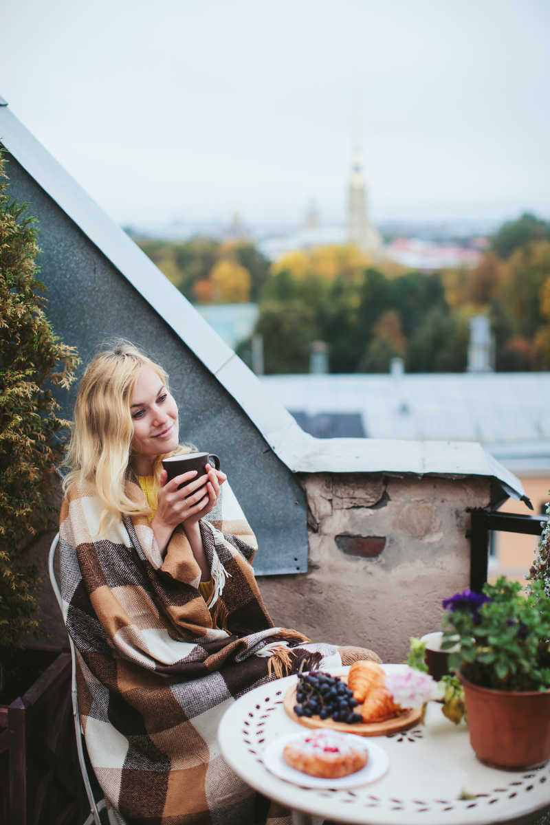 城市建筑背景下在阳台上喝咖啡的金发美女