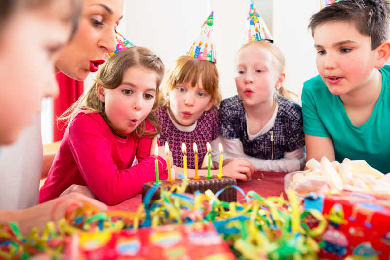 生日派对上孩子们在朋友和母亲的帮助下吹灭蛋糕上的蜡烛