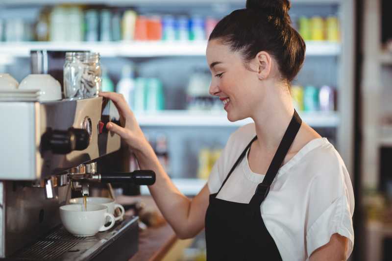 微笑的女服务员实用咖啡机制作咖啡