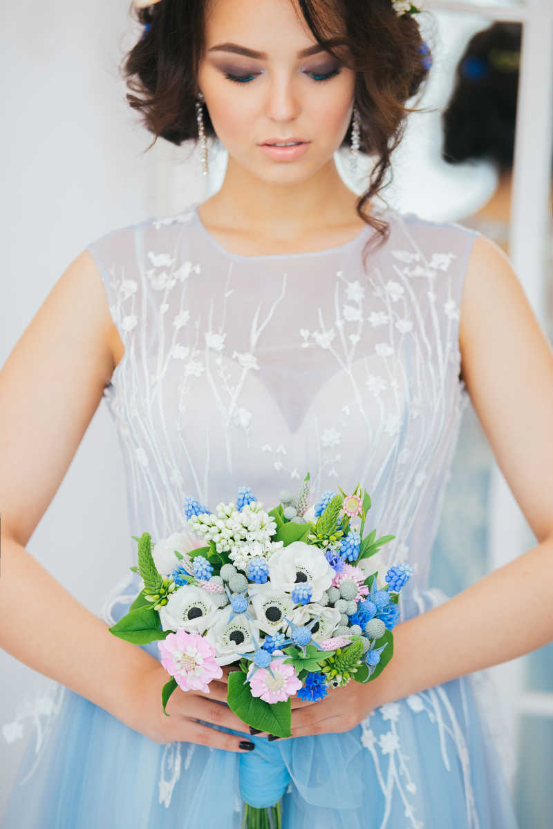 穿着淡蓝色纱裙的新娘双手捧着婚礼花束