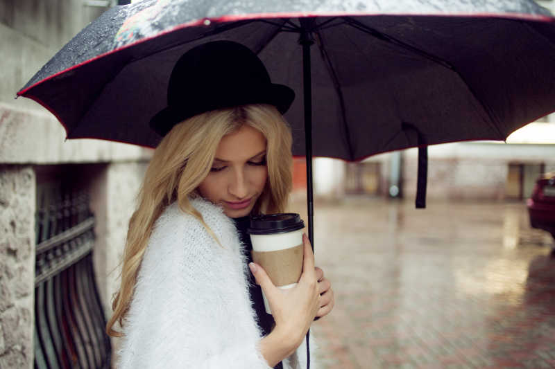 街上撑着伞的女人抱着咖啡杯