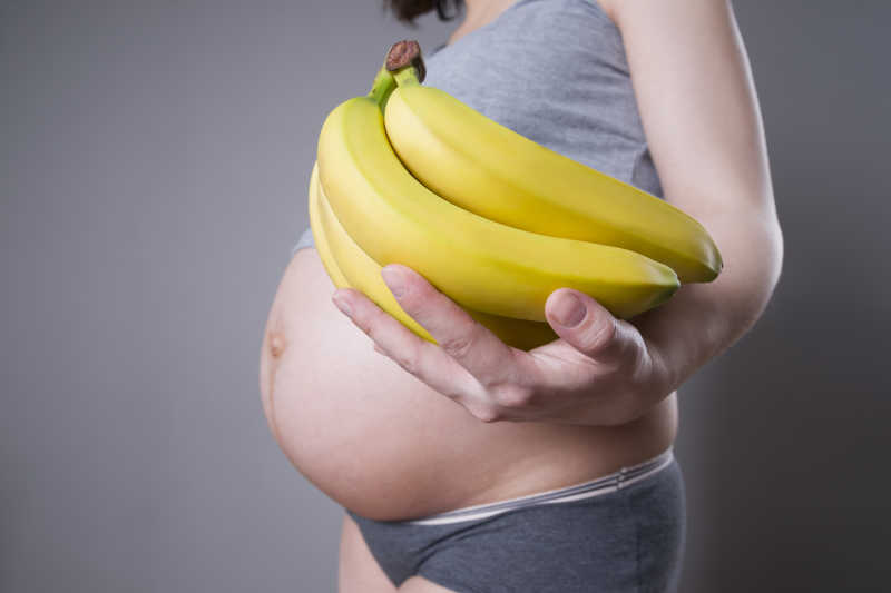 孕妇在灰色背景下手持香蕉