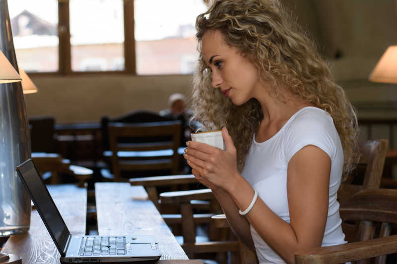 坐在咖啡店的美女手捧咖啡观看电脑