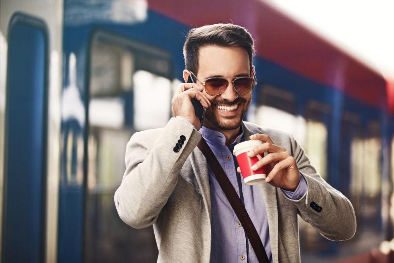 火车站背景前喝着咖啡打电话的男人